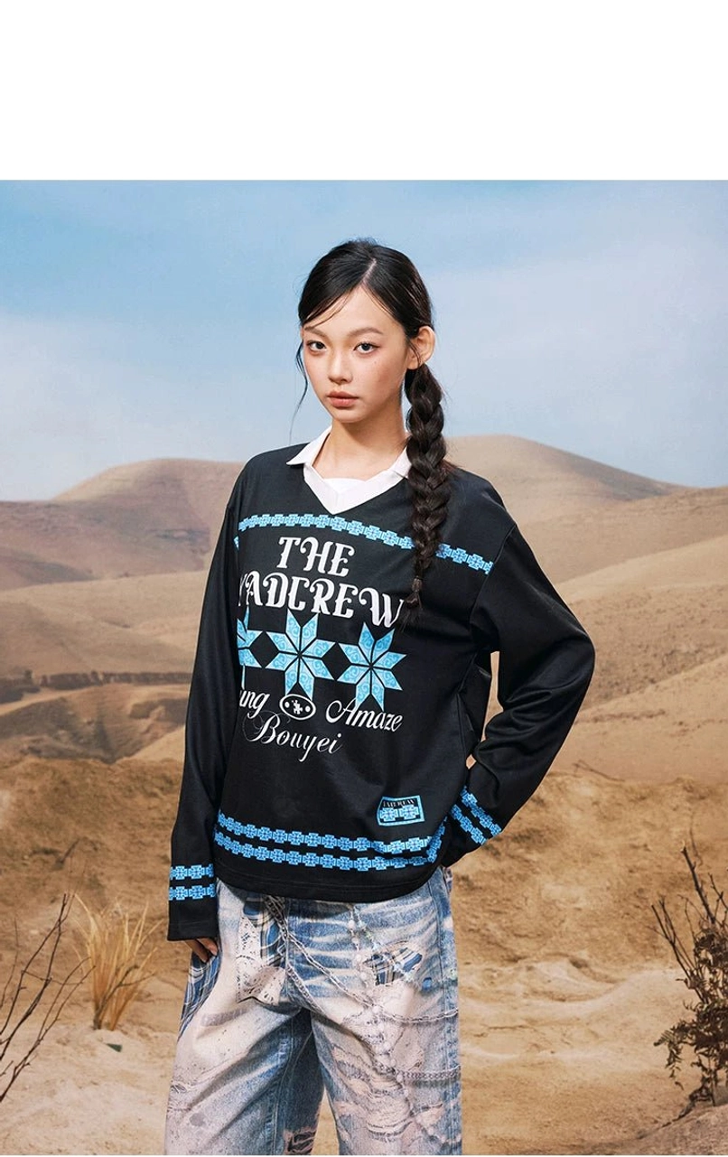 Side three-quarter view of a black oversized geometric graphic polo collar shirt with blue folk-inspired prints and retro sportswear styling