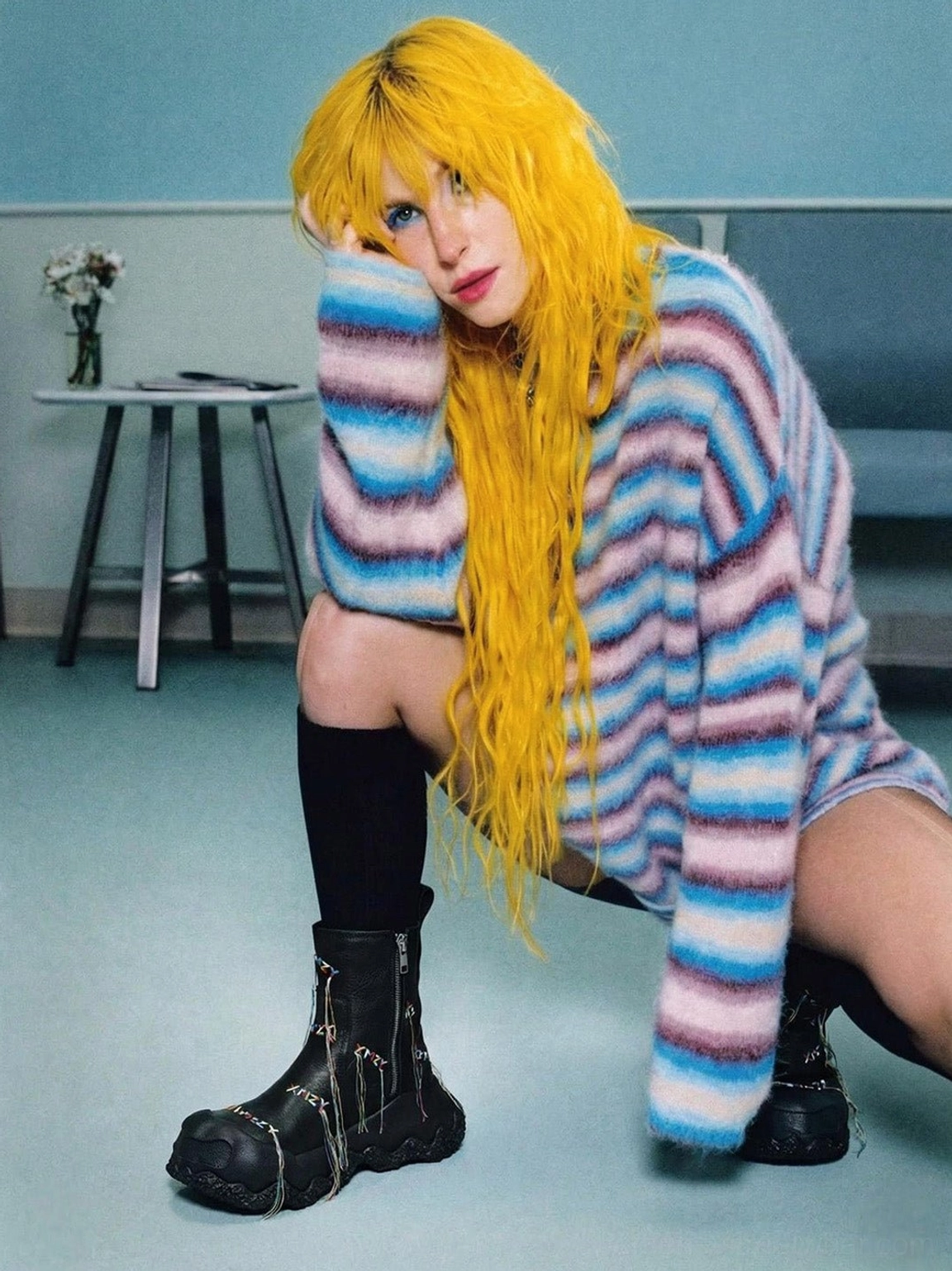 Full outfit styling image of black geometric tassel western ankle boots worn with oversized striped knit sweater in blue lounge studio