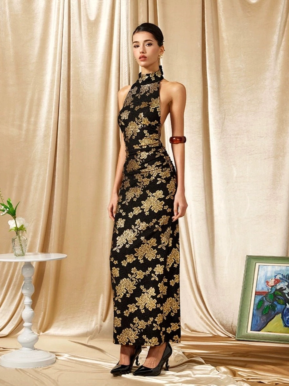 Front full body view of a black and gold floral halter cheongsam maxi dress with high collar fitted silhouette and floor length hem