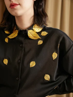 Front upper body view of black golden leaf embroidered oversized streetwear shirt against warm brown curtain backdrop