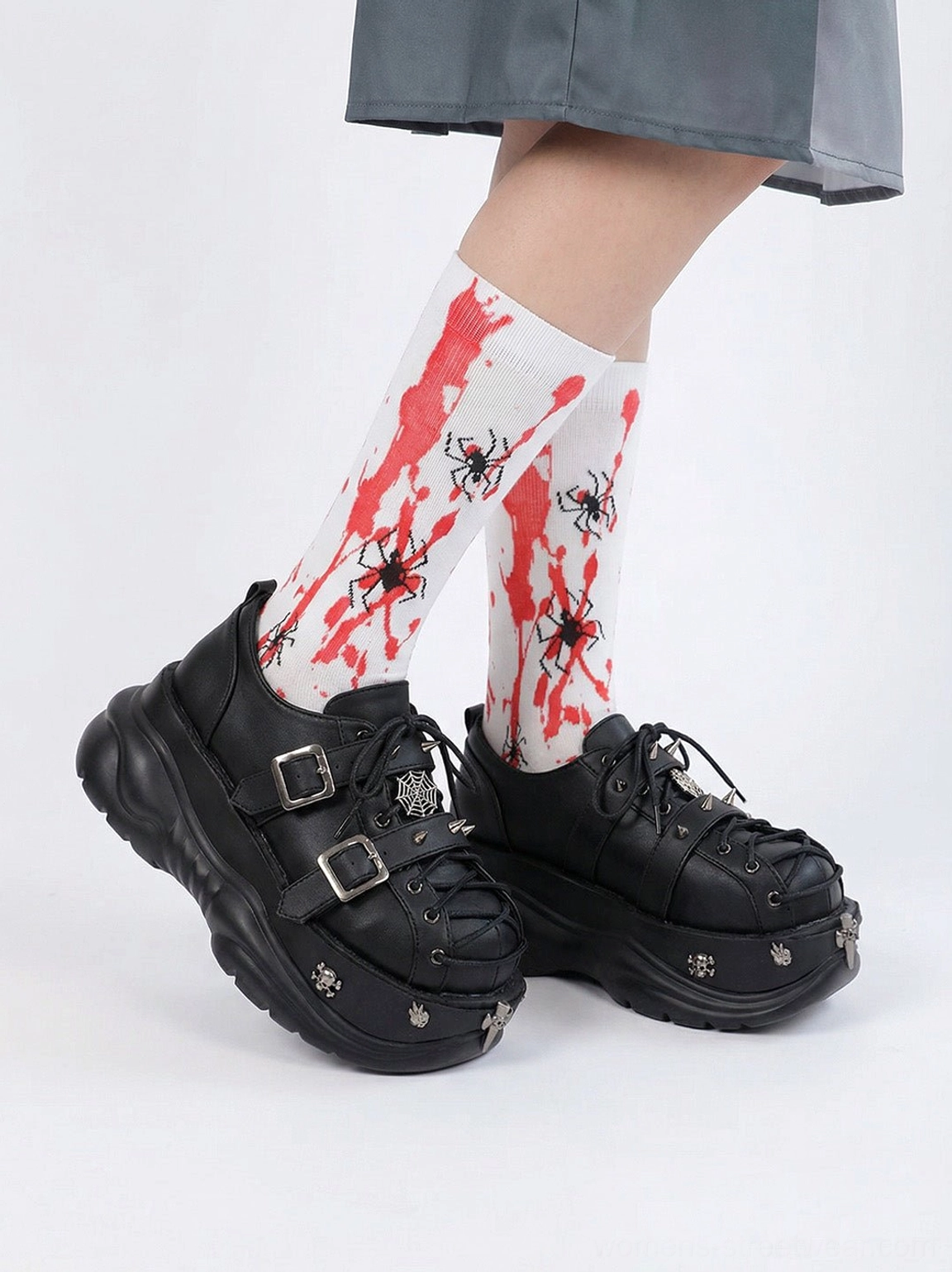 Black gothic buckle sneakers with cross toe charms and chunky platform soles styled with a gray skirt and printed spider socks