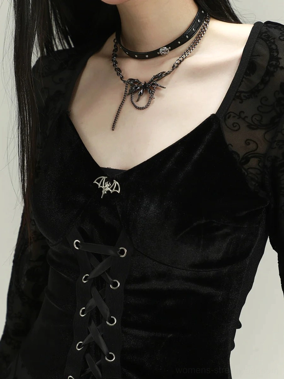 Close-up of black gothic dress sweetheart velvet neckline, metal bat brooch, corset lace-up eyelets and sheer floral lace panels