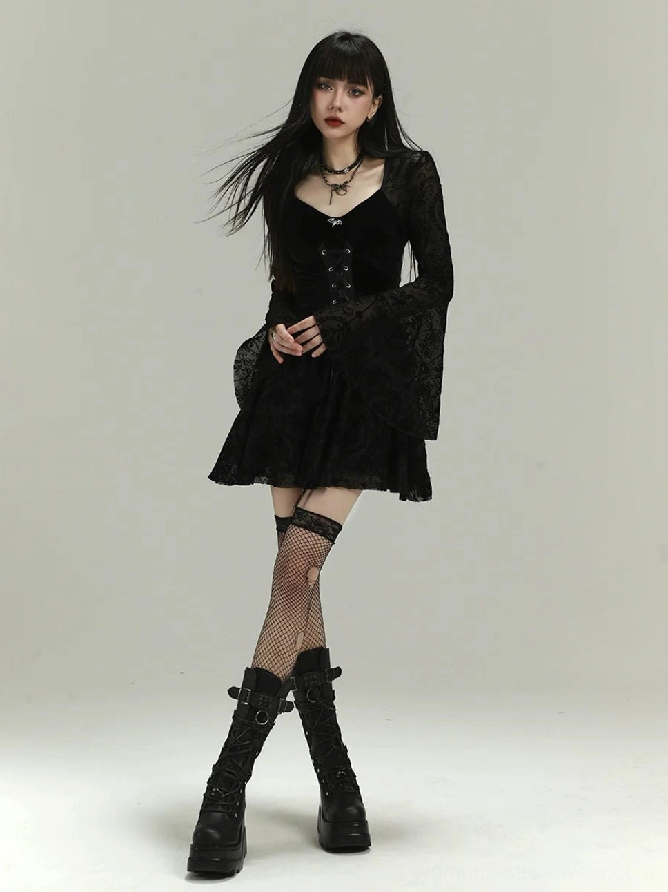 Full body styling view of black velvet gothic mini dress with corset lacing, bell sleeves, fishnet stockings and platform boots