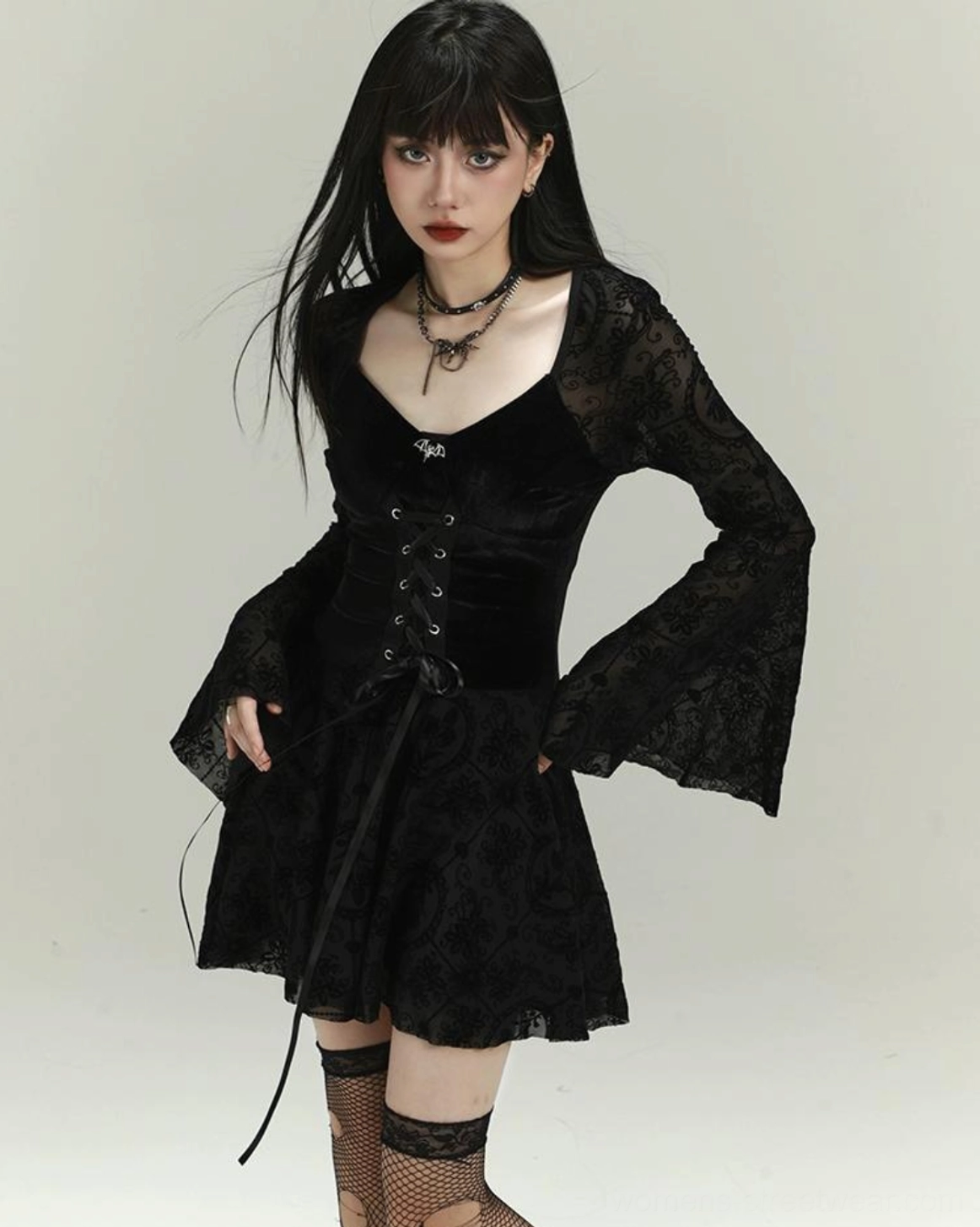 Three-quarter side view of black gothic velvet lace-up mini dress with flared lace sleeves, asymmetric hanging lace-up strap and ruffle hem