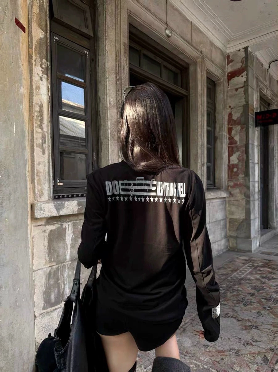 Black fitted gothic long sleeve top shown from the back with star pattern artwork and Do It Everything Well graphic in a vintage architectural setting