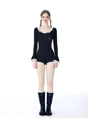 Front view of a black gothic ruffle knit romper with white trim, long sleeves, fitted ribbed silhouette, and black boots