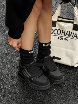 Black gothic streetwear sneakers worn with black crew socks on an asphalt road beside a printed canvas tote bag