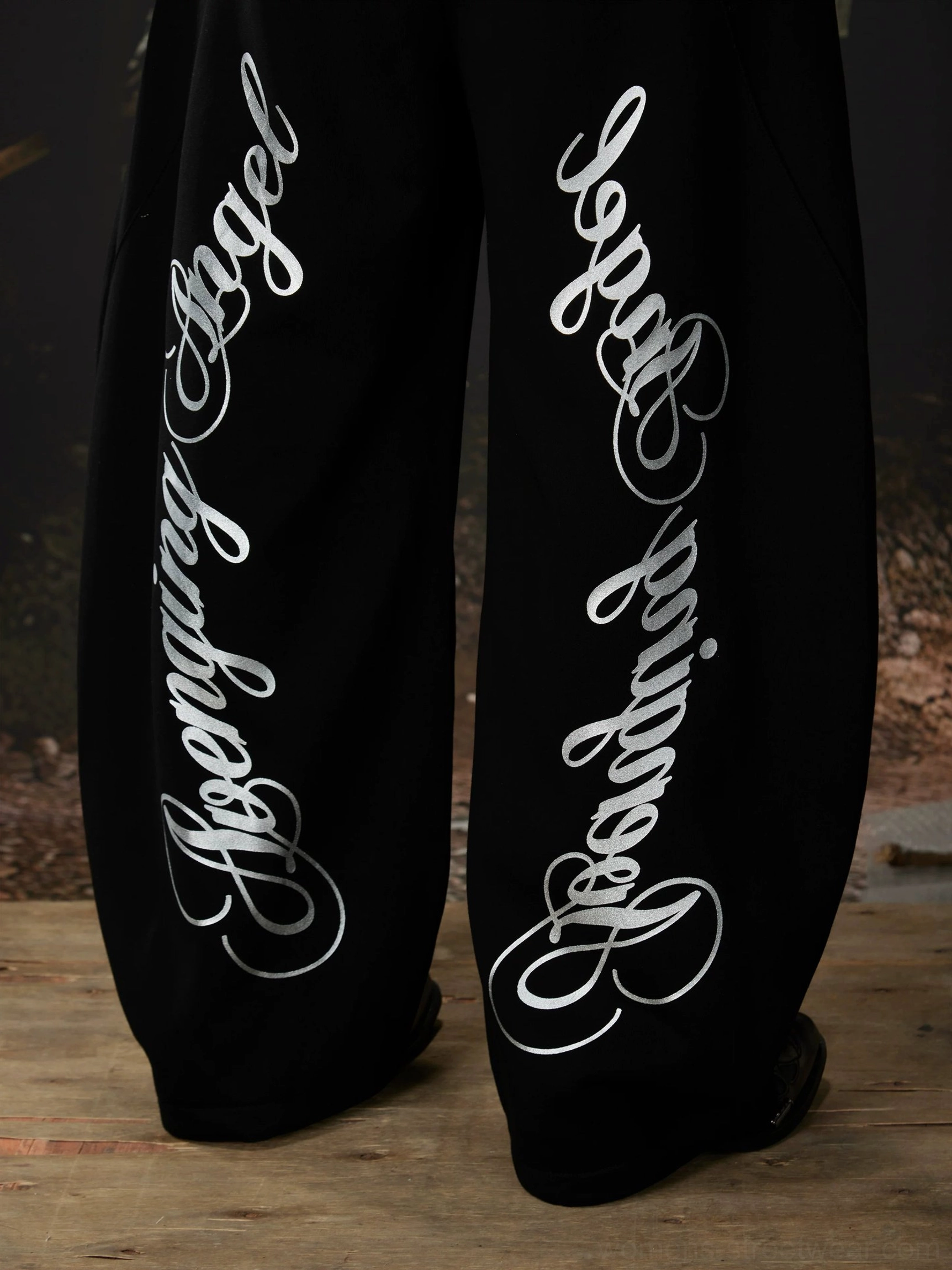 Close-up of black sweatpants legs featuring white cursive gothic script lettering and smooth knitted sweatshirt material