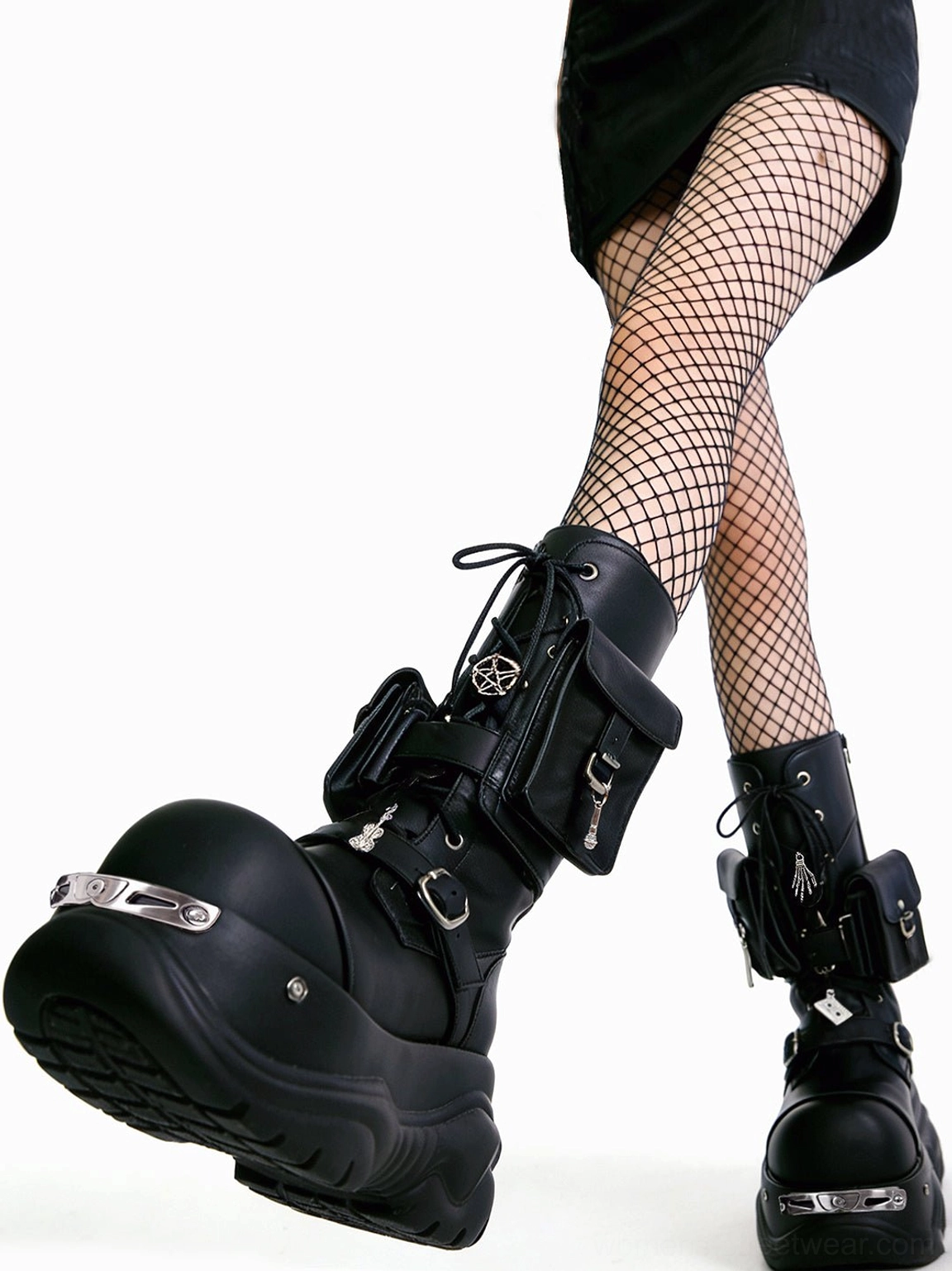 Low front angle of black gothic platform combat boots styled with fishnet tights, metal toe strips, pentagram ankle details, and utility pockets