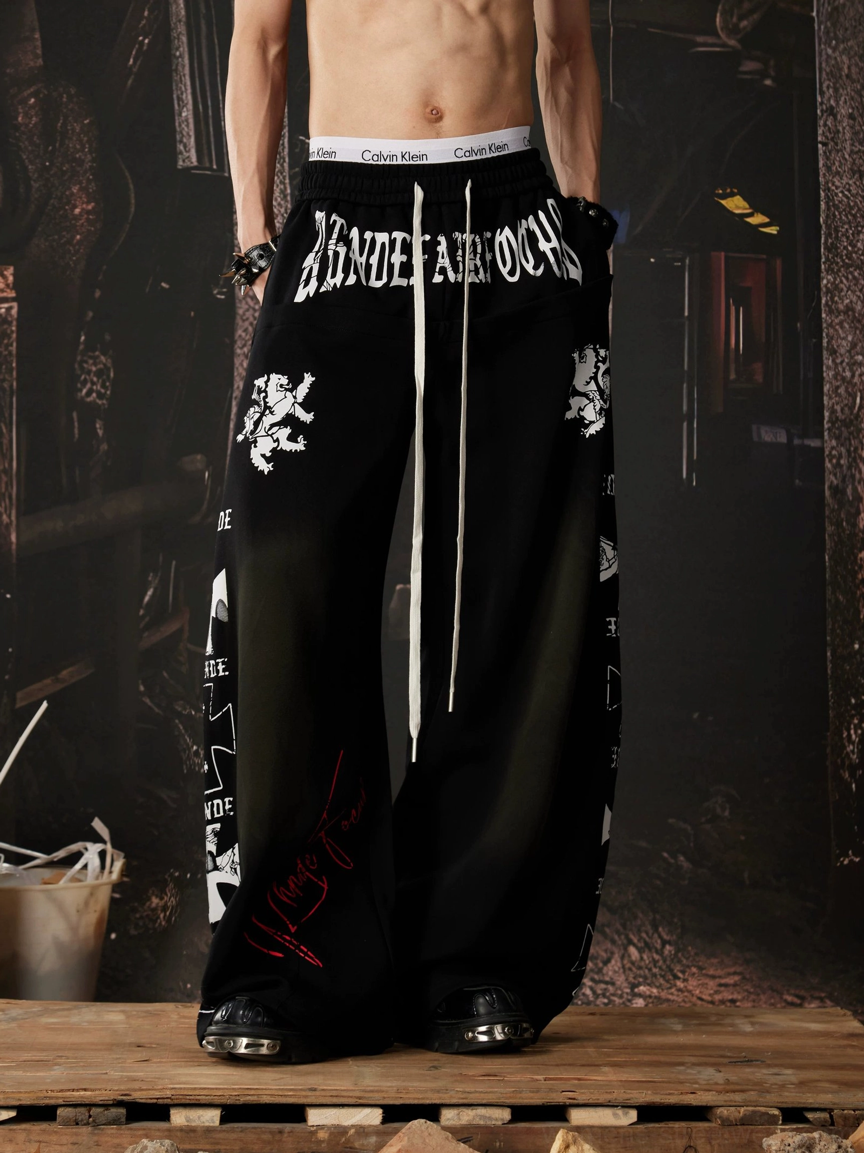 Black gothic wide leg streetwear sweatpants with mixed lettering and heraldic prints, side pocket, drawstring waist, and ultra-loose fit