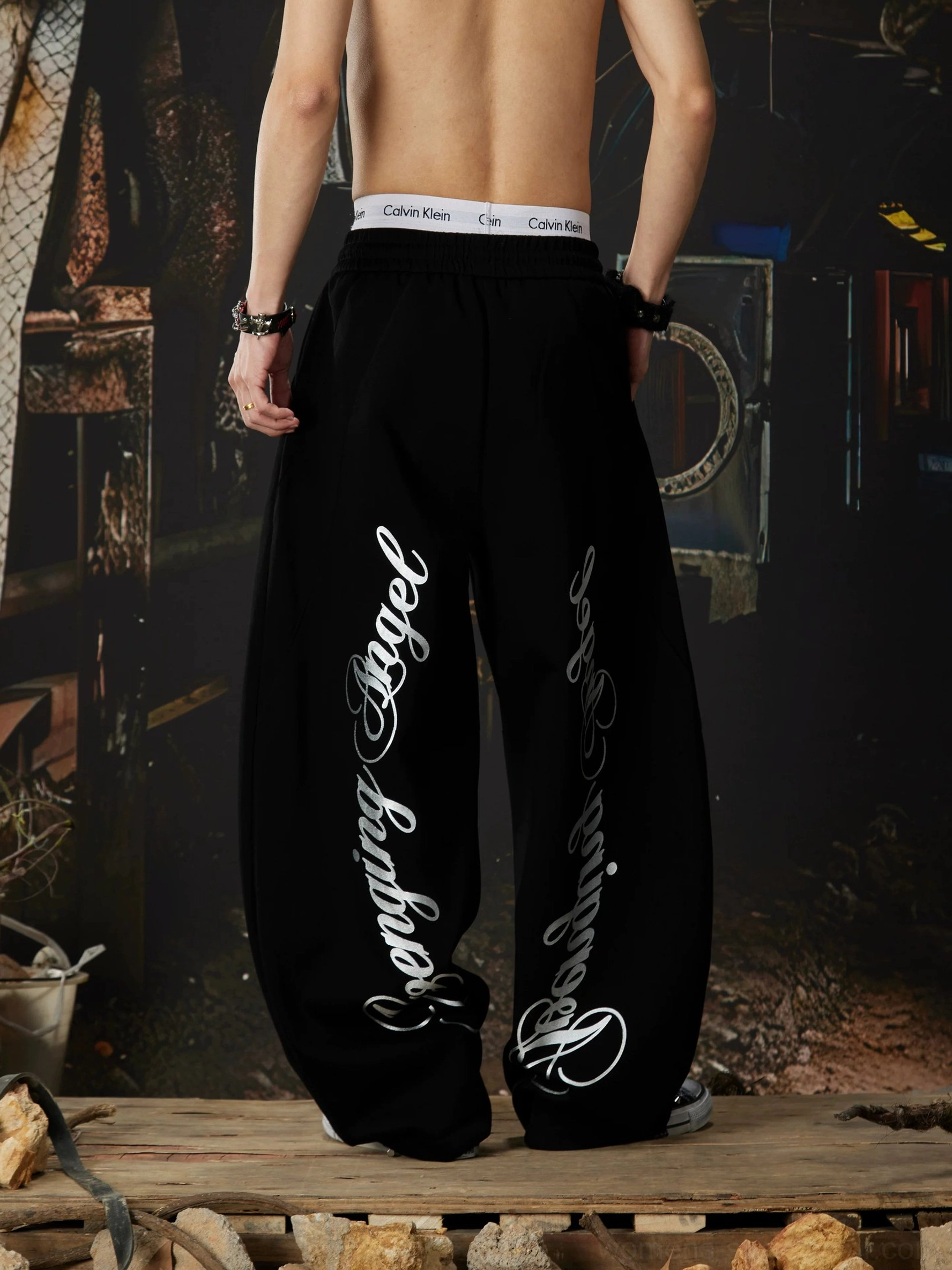 Black gothic wide-leg sweatpants back view with cursive lettering along both outer legs and elastic streetwear waistband