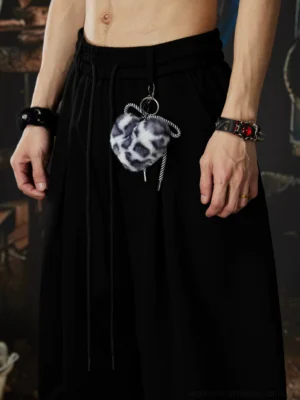 Close-up of black gothic streetwear pants showing front pleats drawstring waistband smooth sweatshirt fabric and fuzzy leopard charm