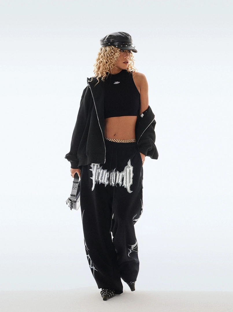Black gothic Y2K streetwear sweatpants styled with cropped top and oversized jacket, featuring wide stacked legs, front graphic, and thorn-inspired side details