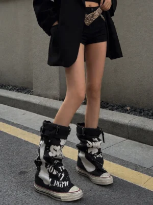 Model wearing black graffiti mid-calf canvas boots with all-black streetwear outfit and leopard waist chain on an urban street