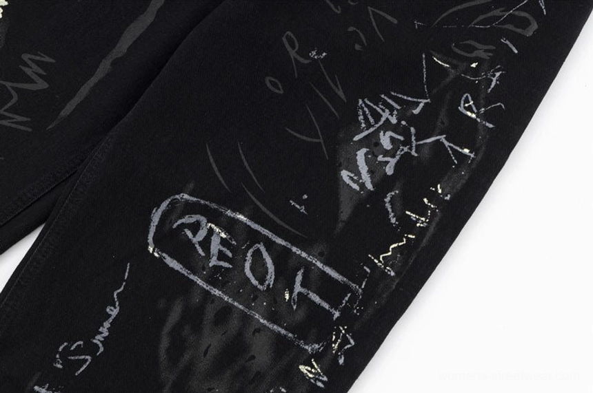 Close-up of layered graffiti lettering and light paint splatter artwork on black wide-leg Y2K denim jeans