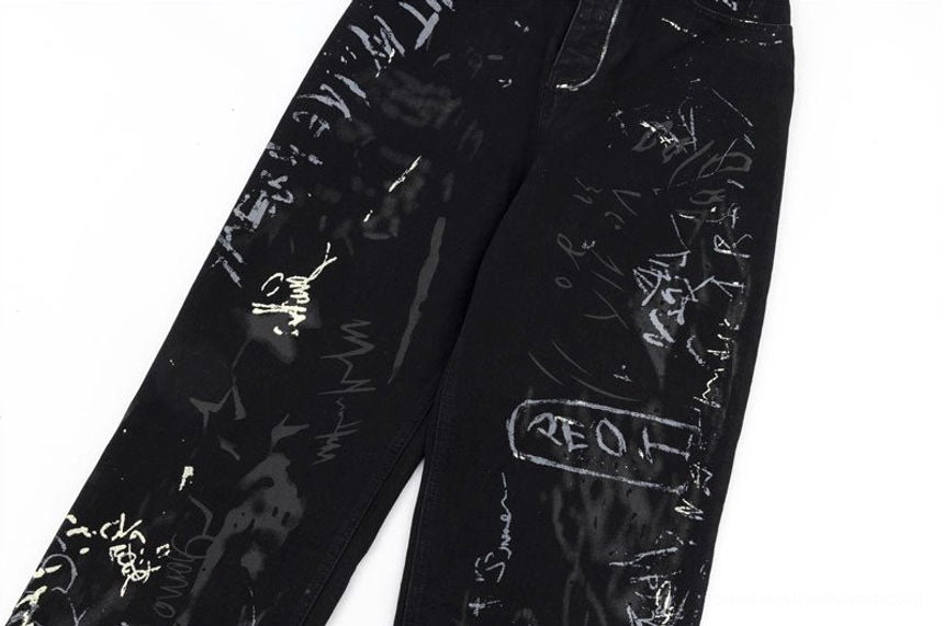 Close-up of wide-leg hems on black graffiti print denim jeans showing white script artwork and paint splatter pattern