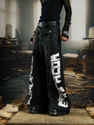 Black graffiti script wide leg streetwear denim pants shown from a low front three quarter angle in an industrial studio