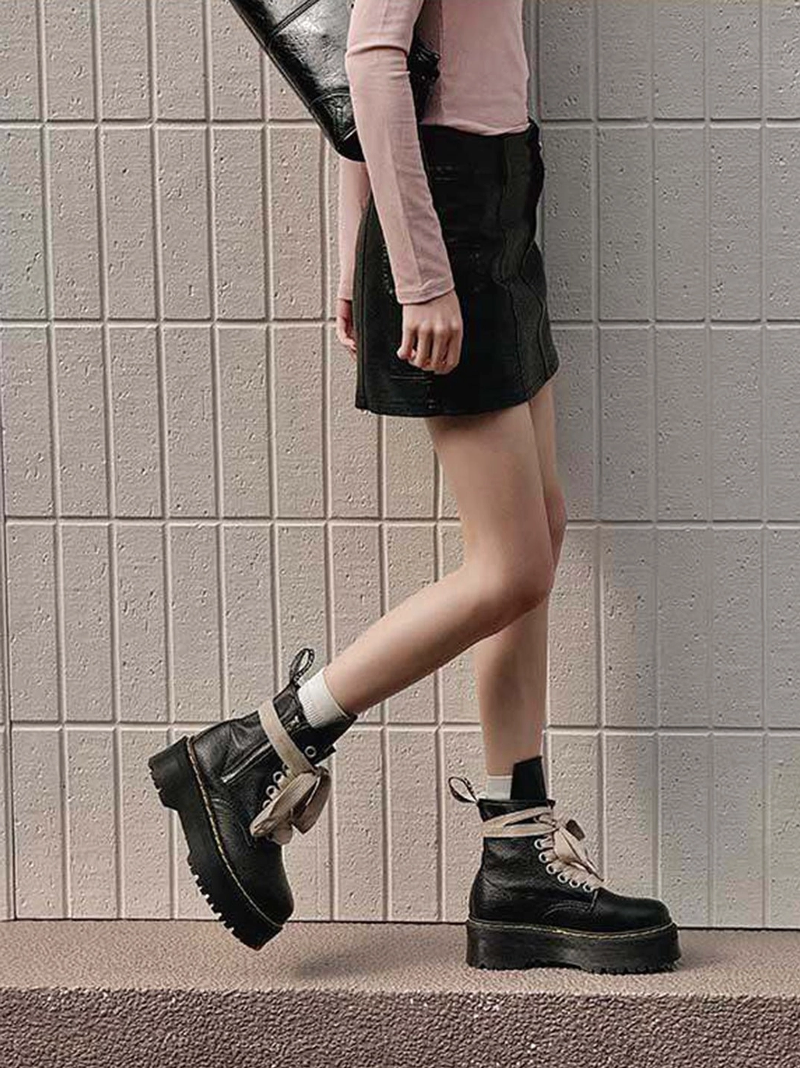 Side profile of black grained leather-look chunky combat boots with wide cream laces and a high-top platform silhouette