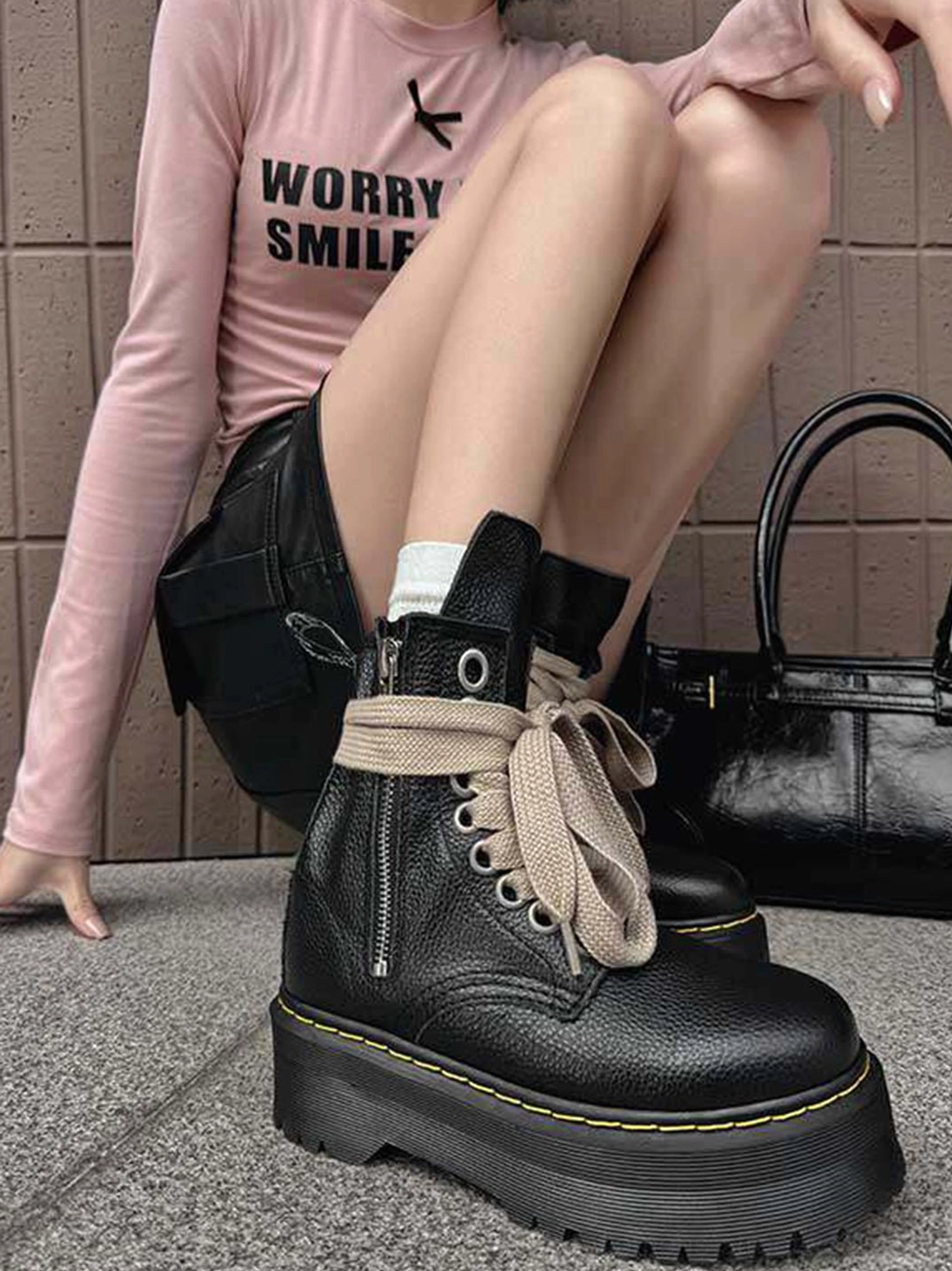 Three-quarter view of black grained platform combat boots with oversized cream laces, side zippers, and contrast yellow sole stitching