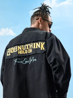 Male model wearing a black oversized cotton button-up shirt with yellow and white embroidered-style back graphics and handwritten lettering