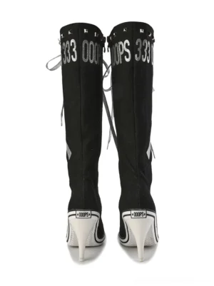 Pair of black graphic print knee-high boots shown from the back with mirrored lettering, lace-up details, white heels, and punk streetwear styling