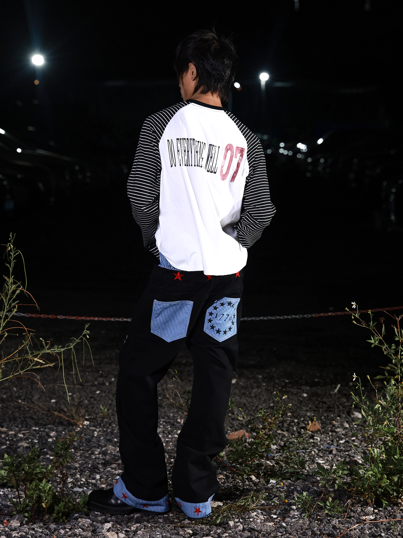 Rear view of black graphic wide-leg jeans with blue striped back pockets, red star waistband details, and bold Korean streetwear-inspired silhouette