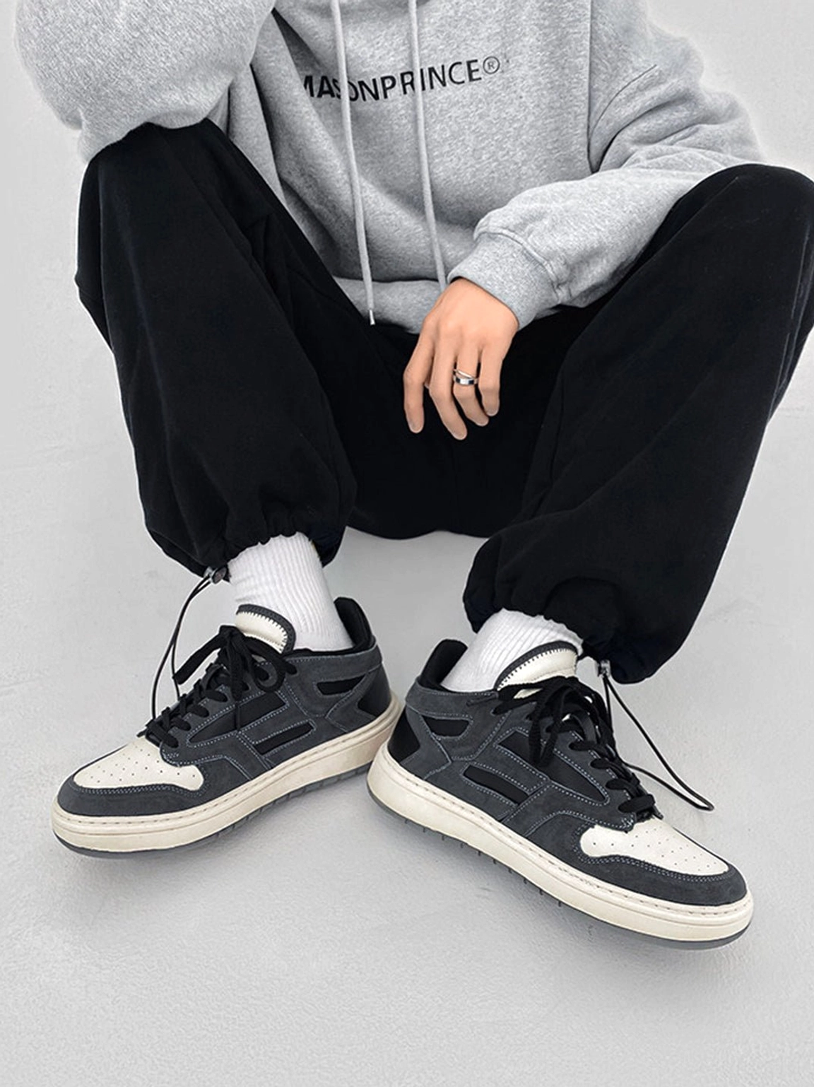 Front view of black and gray low-top streetwear sneakers worn with white socks and black jogger pants while seated