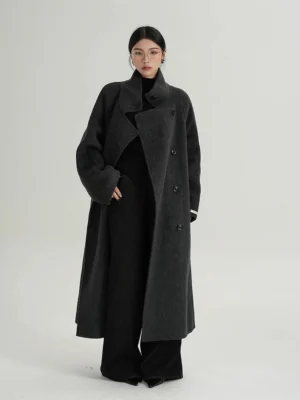 Full-body front view of a woman wearing an oversized dark gray black double-breasted funnel neck wool cocoon coat with dropped sleeves and long streetwear silhouette