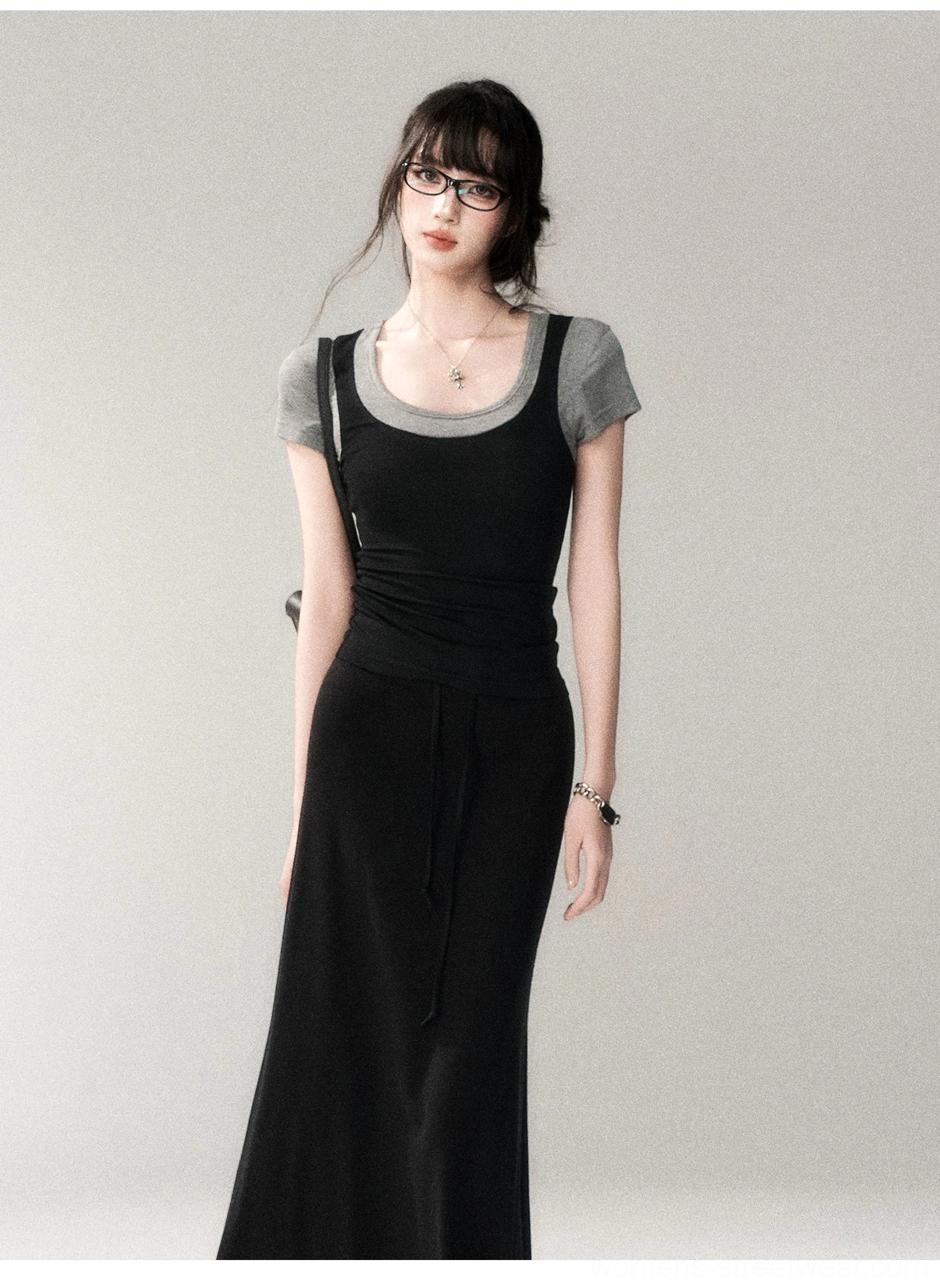 Front three-quarter view of a black and gray contrast scoop neck fitted top layered under a black maxi tank dress with crossbody bag and jewelry