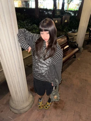 Female model wearing a black and gray striped half-zip cropped hoodie with white typography in an outdoor stone column setting