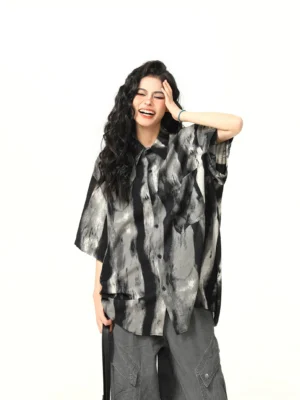 Female model wearing an oversized black and gray watercolor print streetwear shirt with short sleeves and button front in a white studio