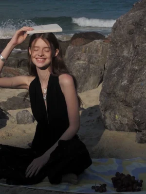 Black halter keyhole peplum top with plunging neckline styled on a model at a rocky beach picnic setting