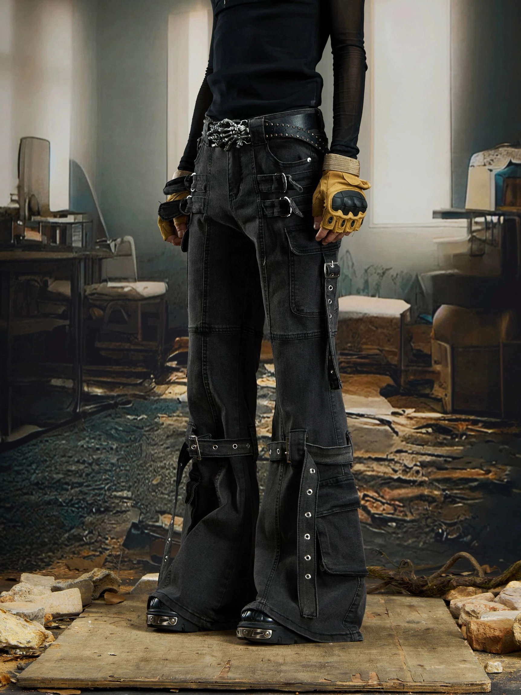 Side three-quarter view of black harness strap cargo jeans showing wide flared legs, thigh and calf straps, metal buckles, and utility streetwear styling
