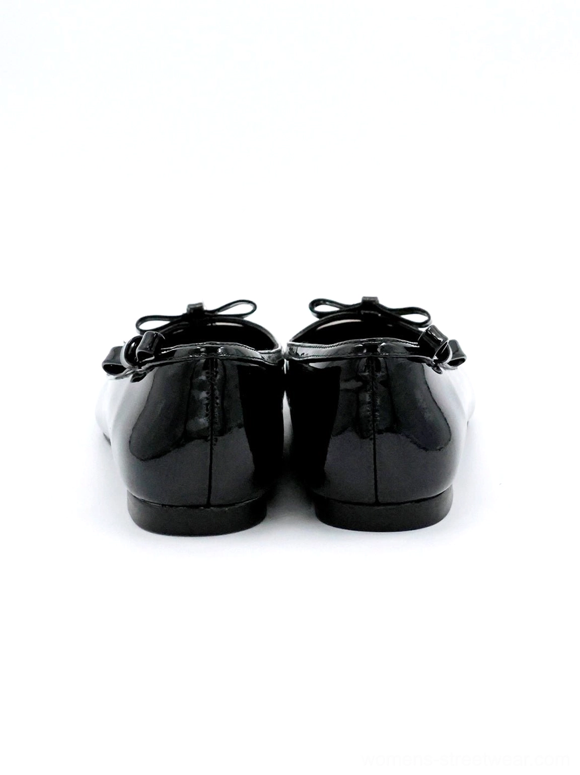 Rear view of black patent ballet flats with glossy finish, heel bow detail, heart-back styling, rounded silhouette, and slim flat sole