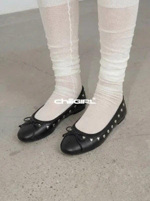 Model wearing black heart-rivet bow ballet flats with off-white stacked socks on a concrete floor, showing a Korean streetwear balletcore styling idea