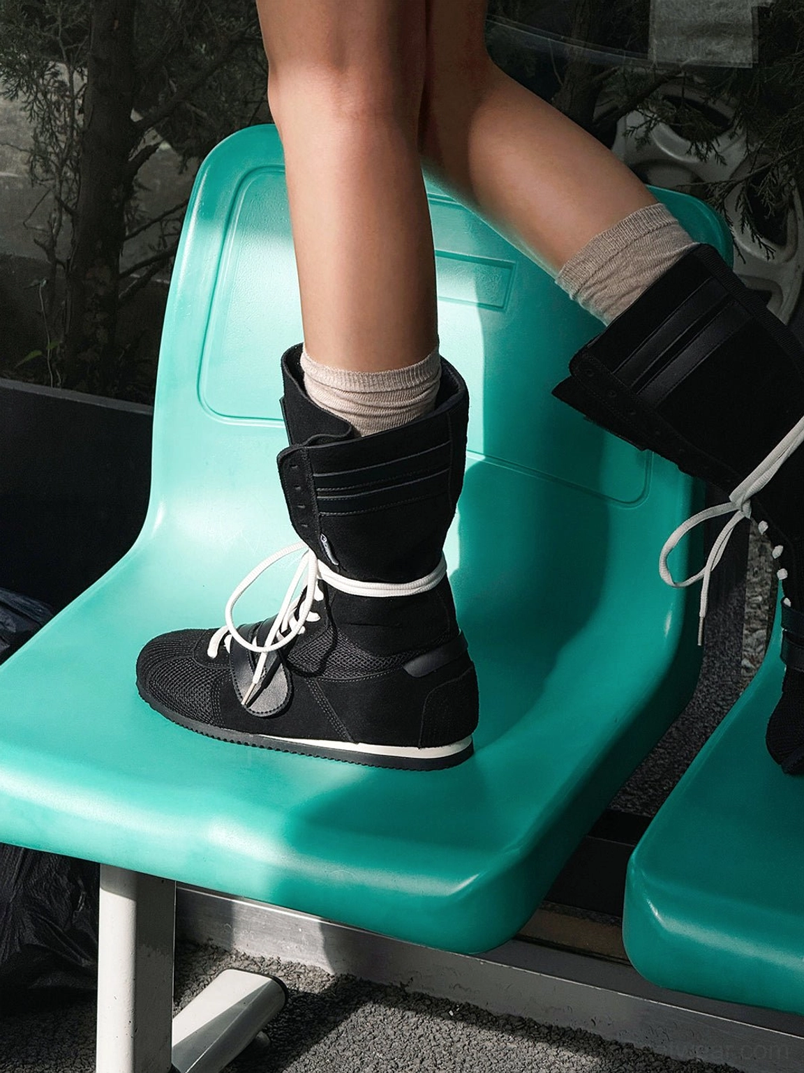 Low-angle view of black high-top boxing boots with white laces and beige crew socks in a casual urban outfit