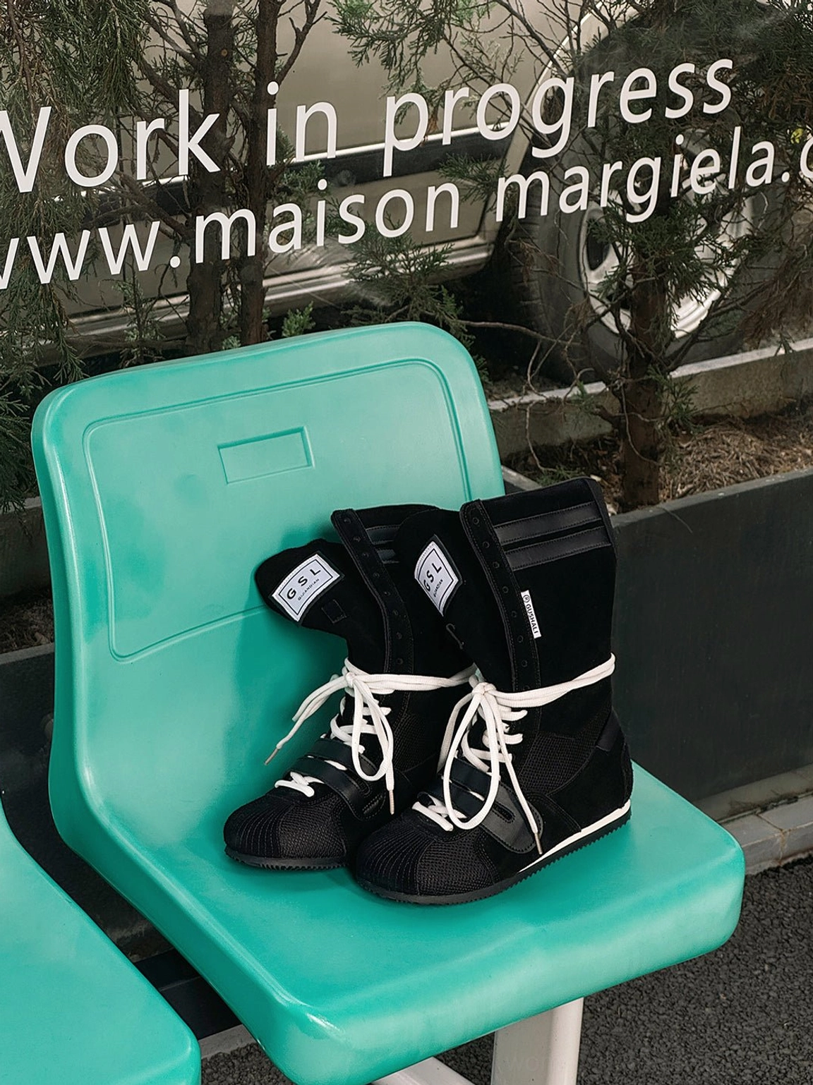 Black high-top boxing-inspired streetwear boots displayed on an outdoor chair with white laces and ankle details