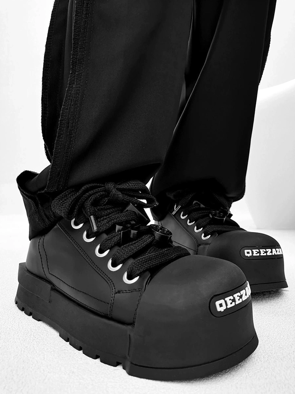 Black high top chunky platform sneakers worn with black straight leg pants showing rugged raised rubber sole