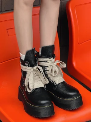 Front view of black high-top platform combat boots with wide cream laces, side zipper closure, rounded toes, and yellow lug sole trim