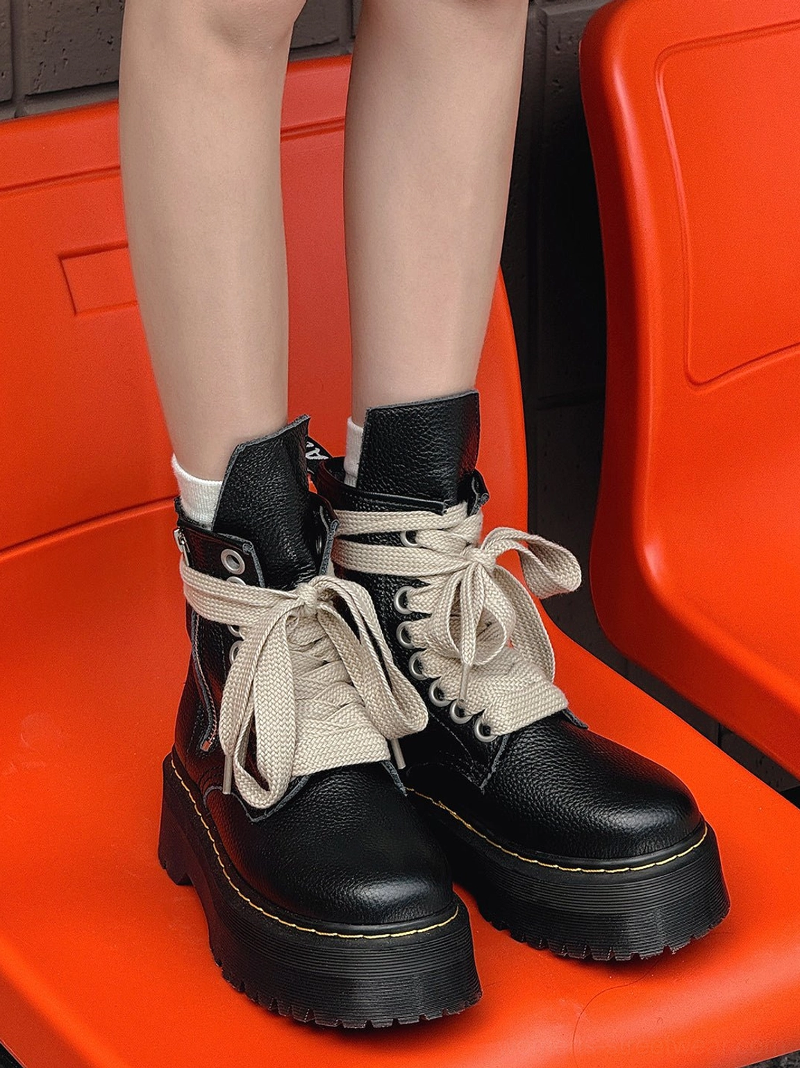 Front view of black high-top platform combat boots with wide cream laces, side zipper closure, rounded toes, and yellow lug sole trim