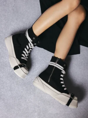 Black high-top platform streetwear sneakers worn on feet with a monochrome outfit, showing the raised white sole and structured ankle-high silhouette