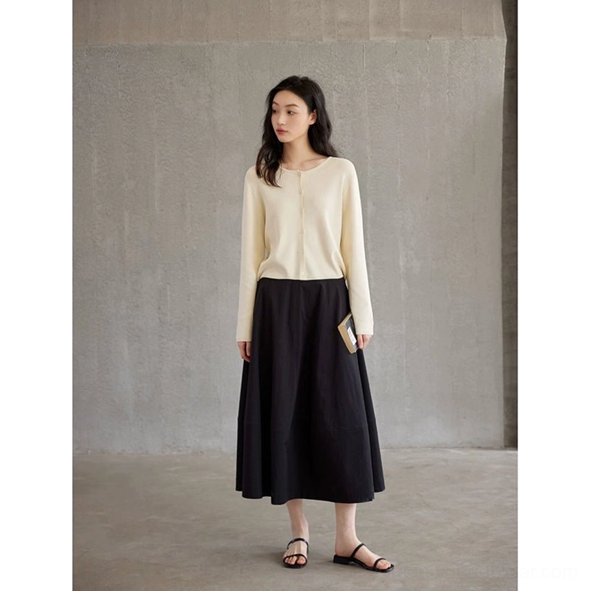 Black high waist A-line floor length maxi skirt styled with a beige long sleeve knit top in a minimalist studio