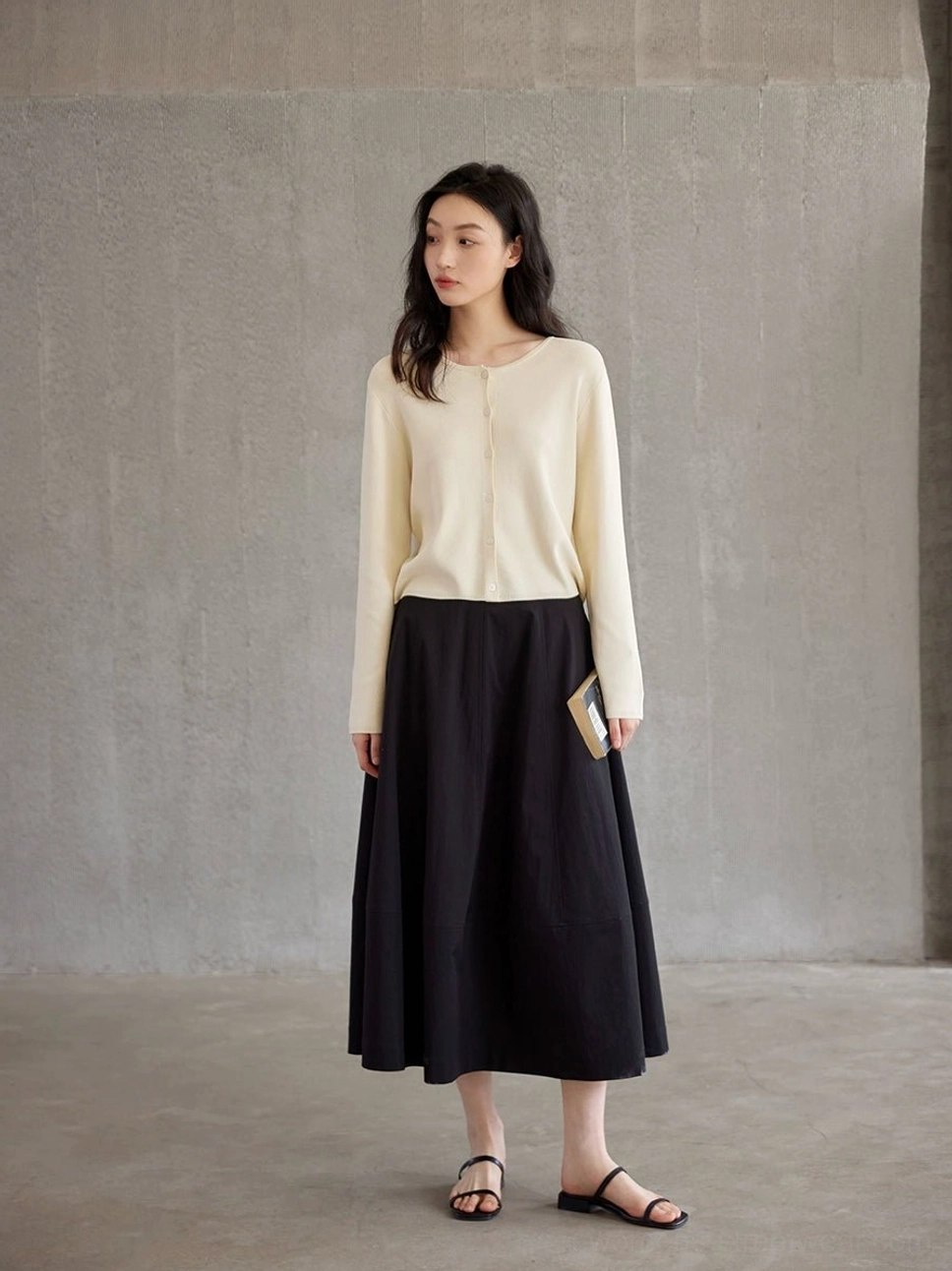 Black high waist A-line maxi skirt styled with a beige cropped knit cardigan in a minimalist concrete studio front view