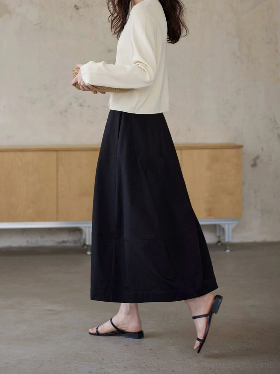 Back view of black high waist A-line maxi skirt showing the clean long flowing silhouette in a concrete studio