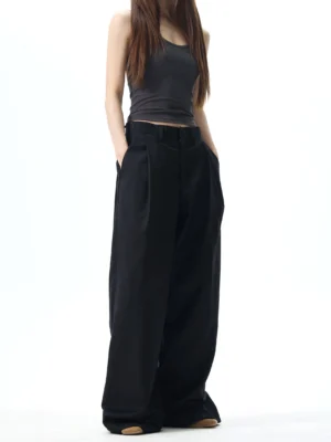 Black high-waisted pleated wide-leg streetwear dress pants shown from the front on a female model with floor-length trousers and side pockets