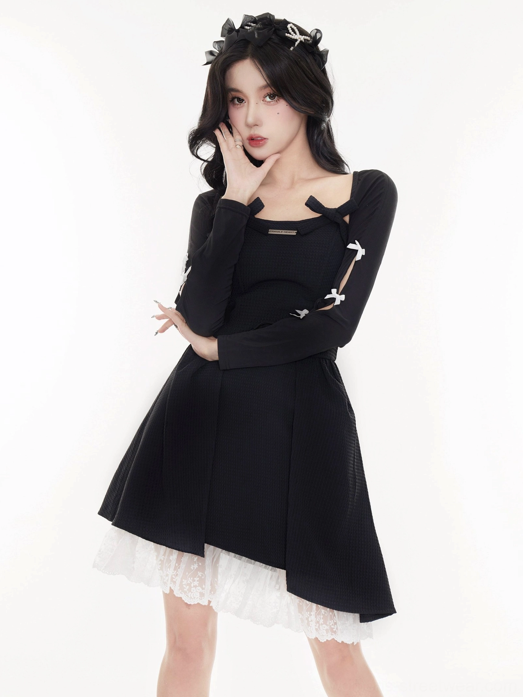 Back three-quarter view of a black cropped cardigan with hollow-out sleeves, white bow accents, and a lace-trimmed layered outfit