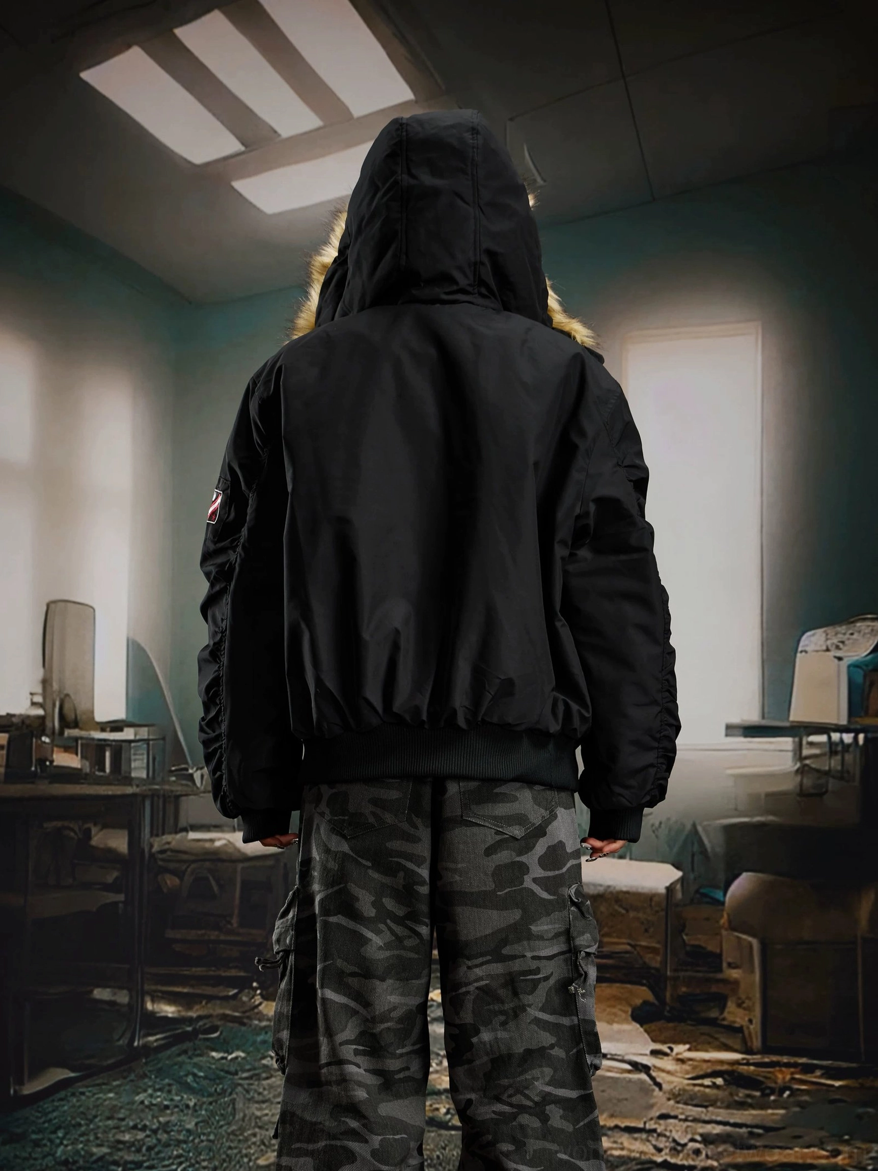 Rear view of a male model wearing a black hooded bomber jacket with a relaxed silhouette and camo cargo pants