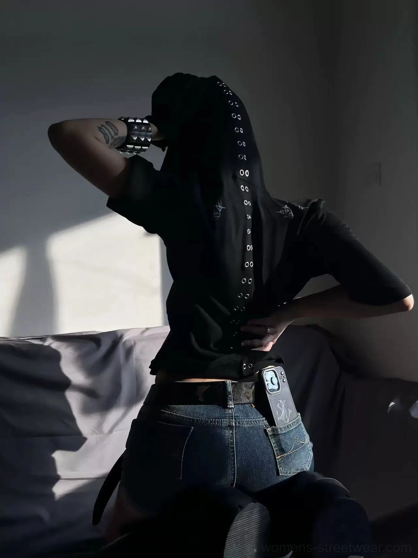 Back view of black short-sleeve hooded tee featuring central metal eyelet trim and cross graphics