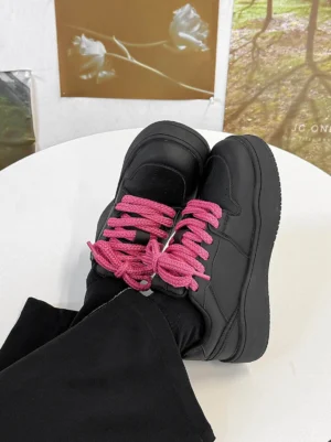 Top-down view of black platform sneakers with bright hot pink contrast laces styled with black streetwear pants