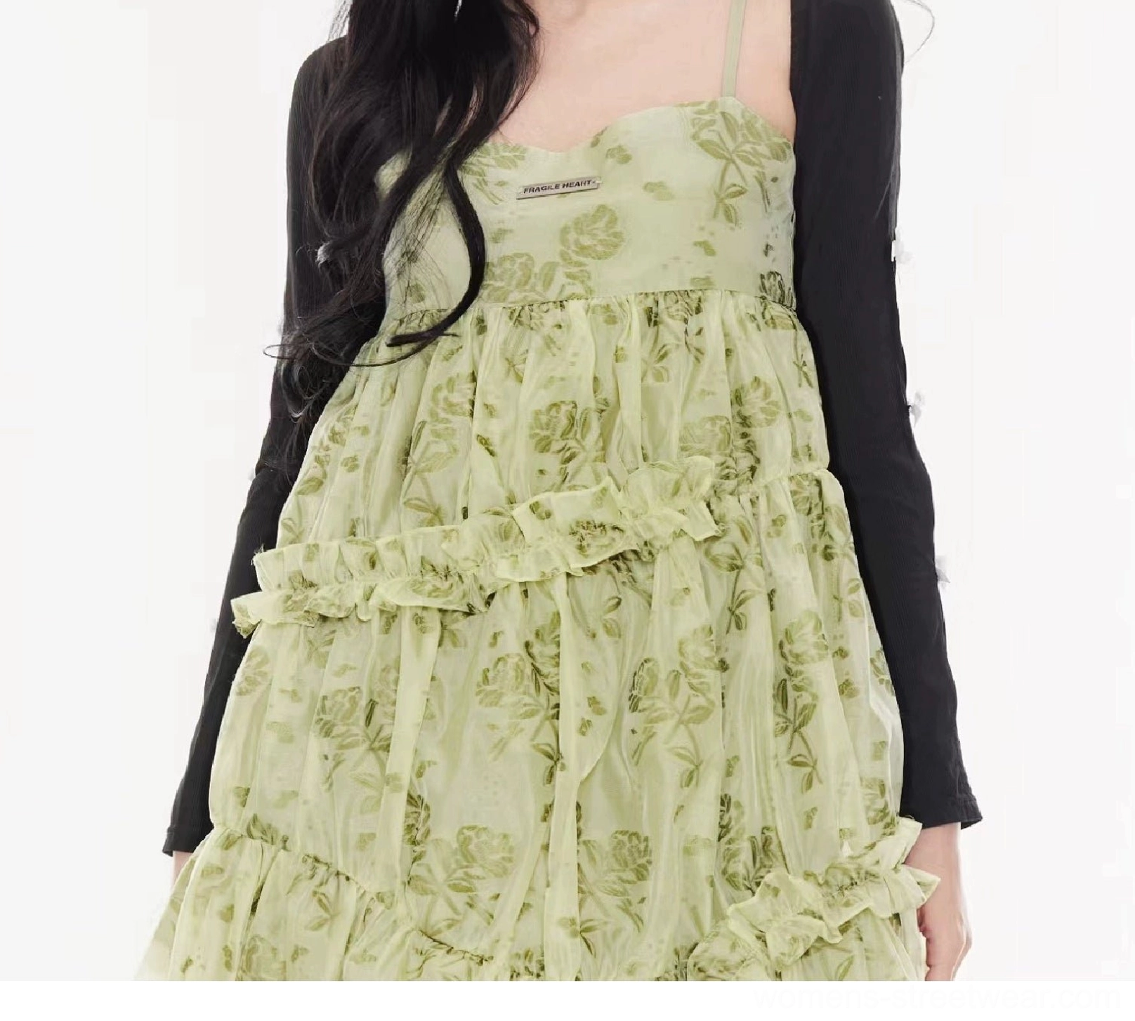 Upper-body styling view of a black cropped cardigan with an irregular hem, bow sleeve slits, and green floral dress layering